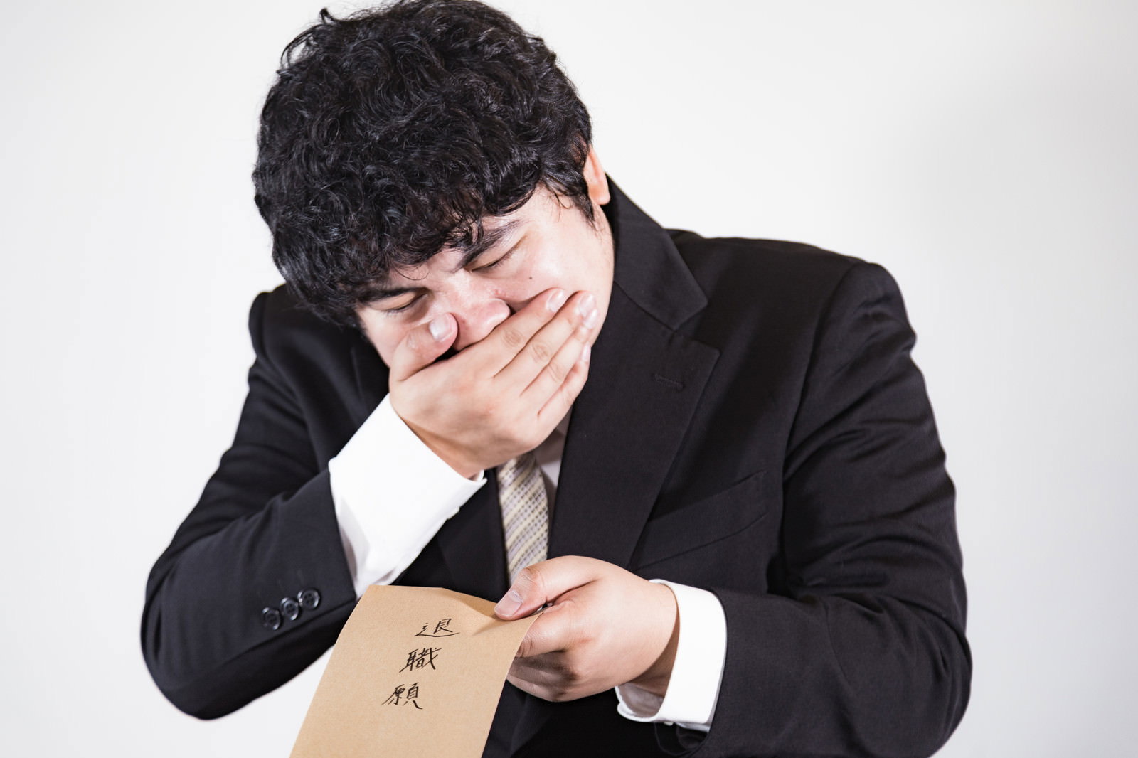 黒いスーツを着て頭を抱えながら書類を持つ困った表情の男性［モデル：段田隼人］