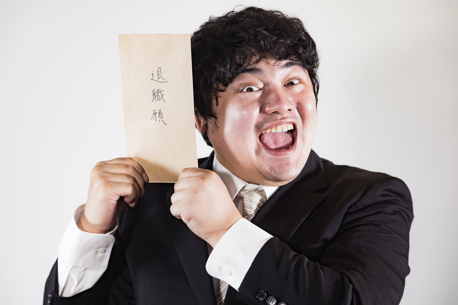 退職願の書類を両手で持ち、大きく笑うスーツ姿の男性［モデル：段田隼人］