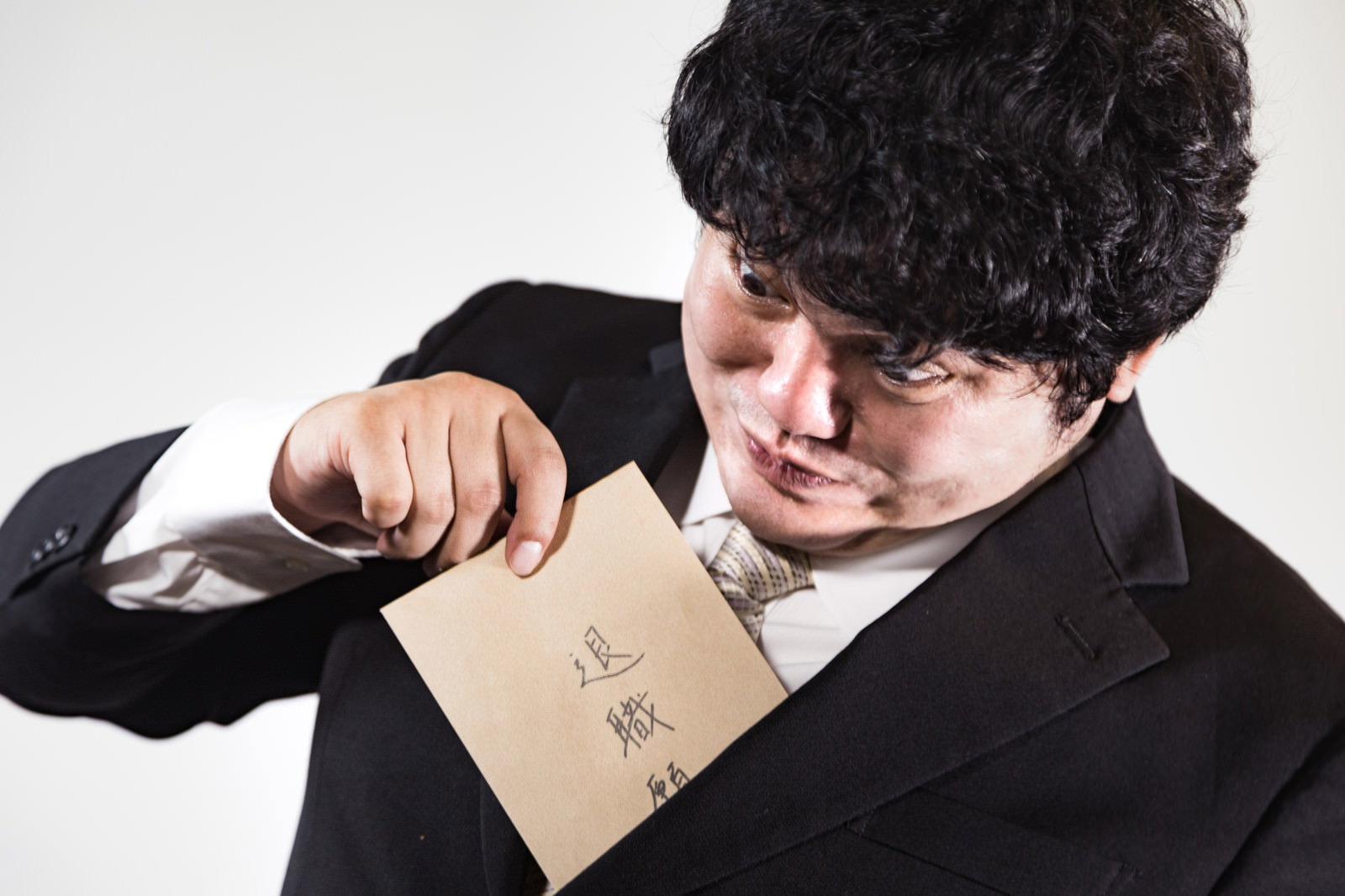 黒いスーツを着た男性が退職願の入った封筒を手に持っている［モデル：段田隼人］
