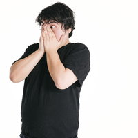 驚きのあまり両手で口を覆う男性のショック表現の写真