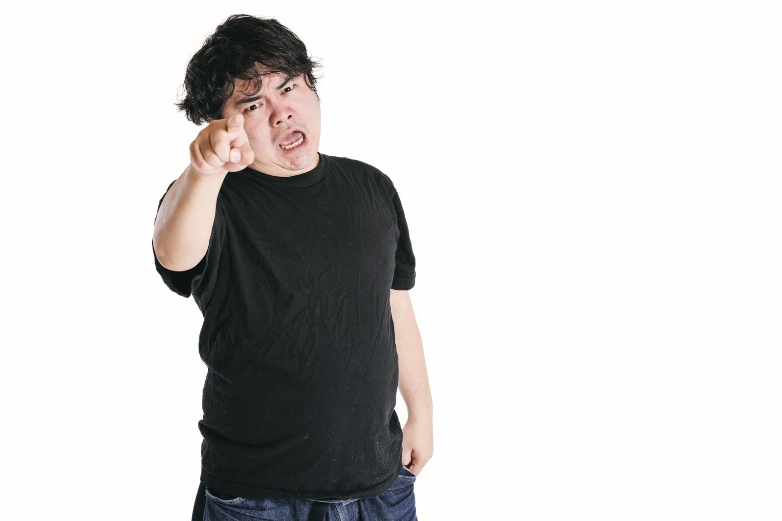 黒いTシャツを着た男性が指を差して威嚇し、厳しい顔で睨んでいる［モデル：段田隼人］