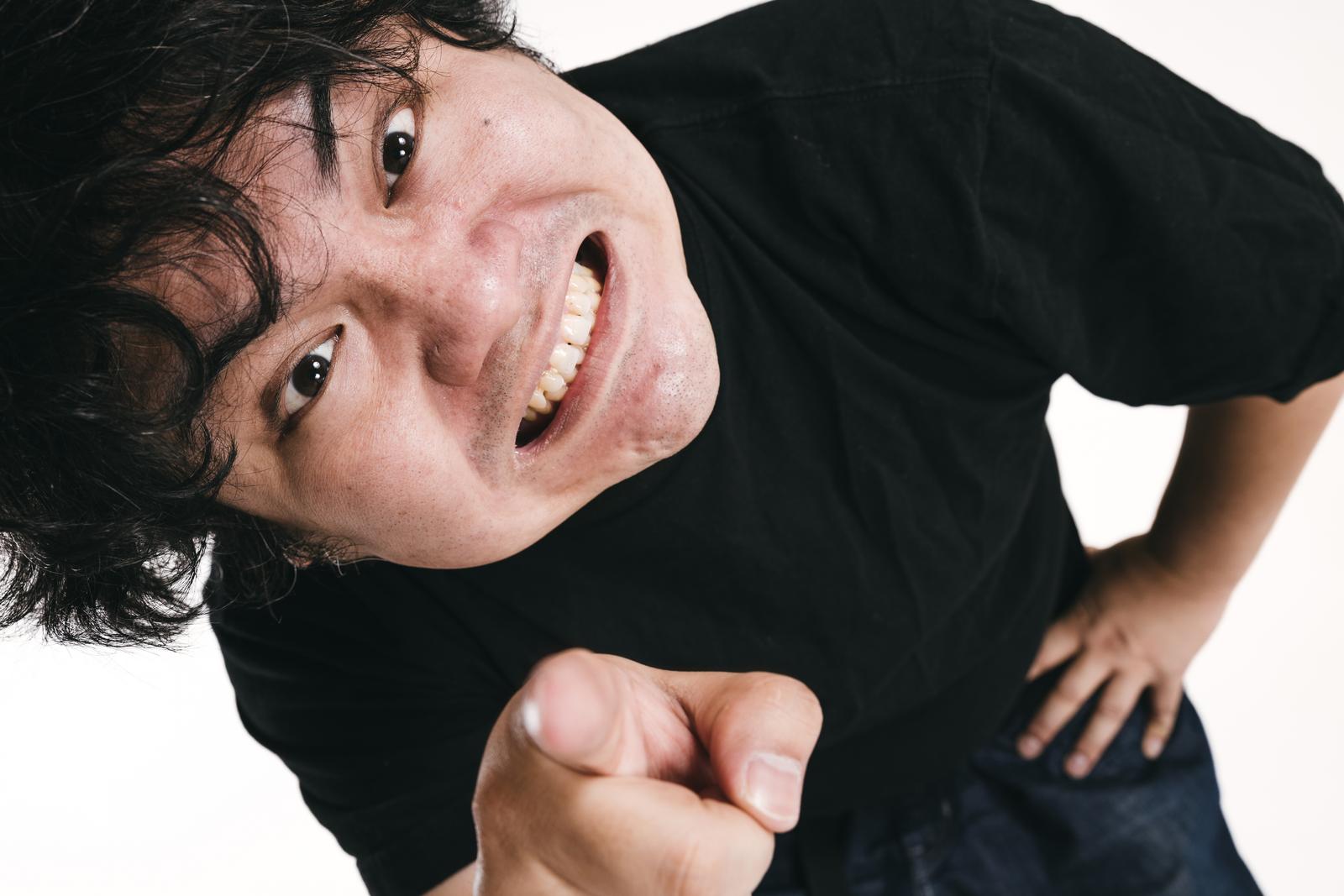 黒いシャツを着た男性が指をさして、からかうような表情をしている［モデル：段田隼人］