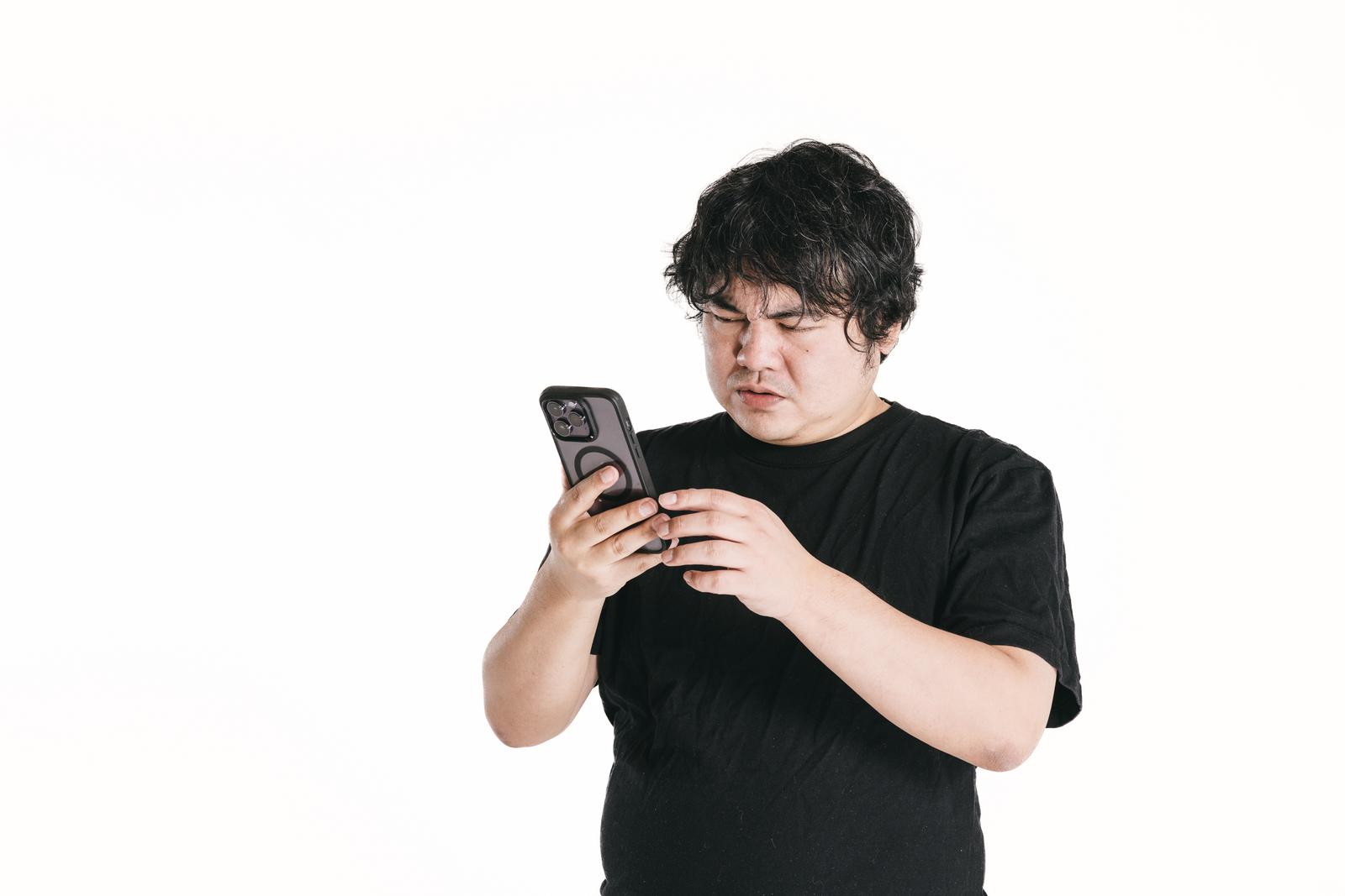 スマートフォンを見つめて困った表情の男性［モデル：段田隼人］