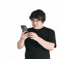 スマートフォンの画面を見つめて悩む黒いTシャツの男性の写真