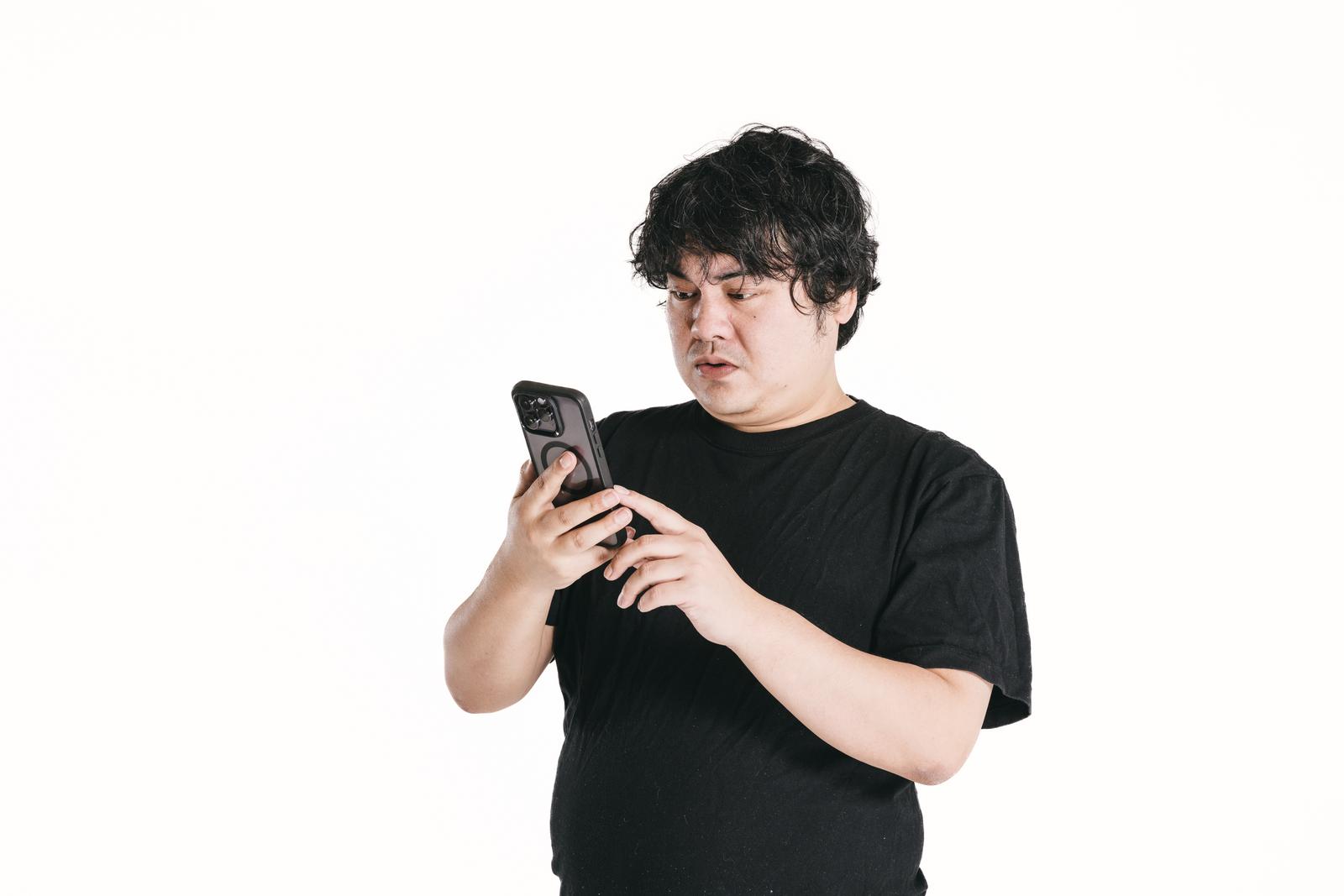 スマートフォンの画面をじっと見つめる黒いTシャツを着た男性［モデル：段田隼人］