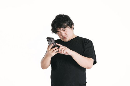 スマートフォンを見つめながら首を傾げる男性