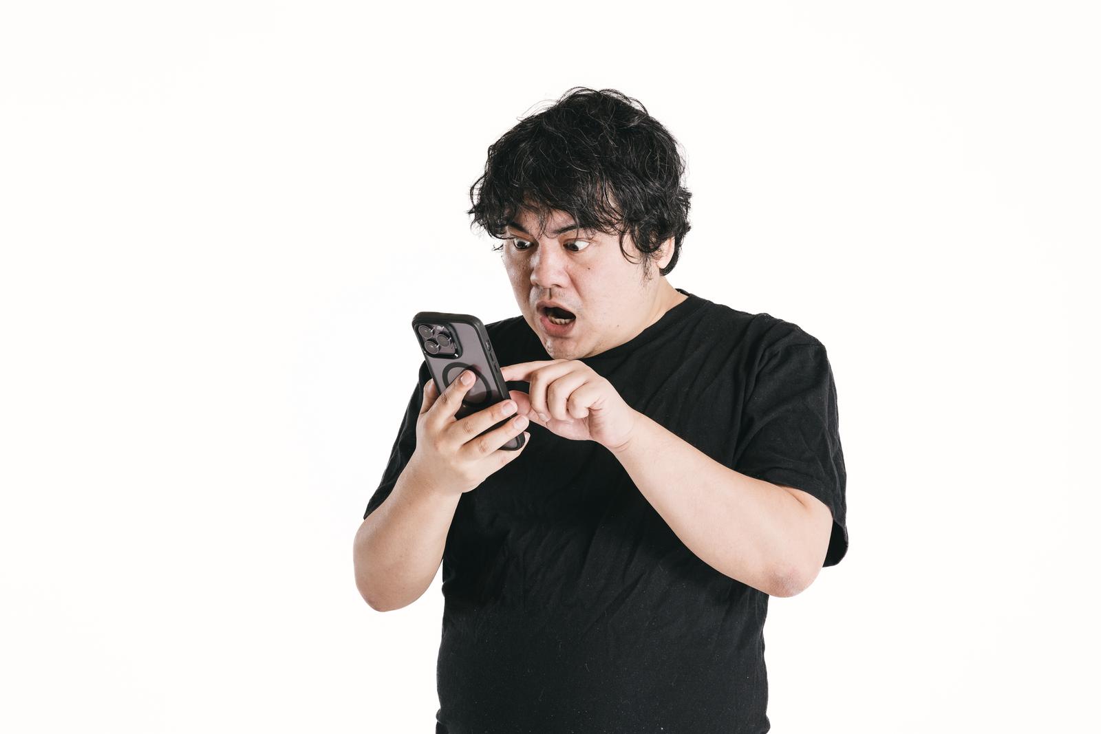 スマートフォンを凝視して驚いた表情の男性［モデル：段田隼人］