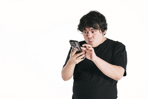 黒いTシャツを着た男性がスマートフォンの画面を凝視して驚く瞬間