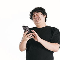 スマートフォンを見ながら苦悩する黒いTシャツの男性の写真