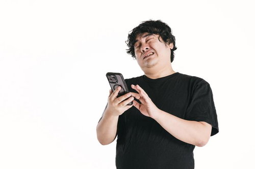 スマートフォンを見ながら苦悩する黒いTシャツの男性