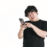 スマートフォンの画面を見ながら苦悩する男性の写真