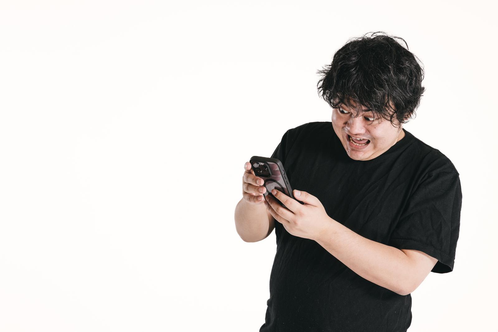 スマートフォンを持って驚く表情の男性［モデル：段田隼人］