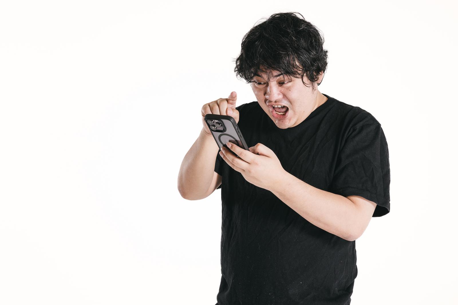 スマートフォンの画面を見て驚く黒いTシャツの男性［モデル：段田隼人］