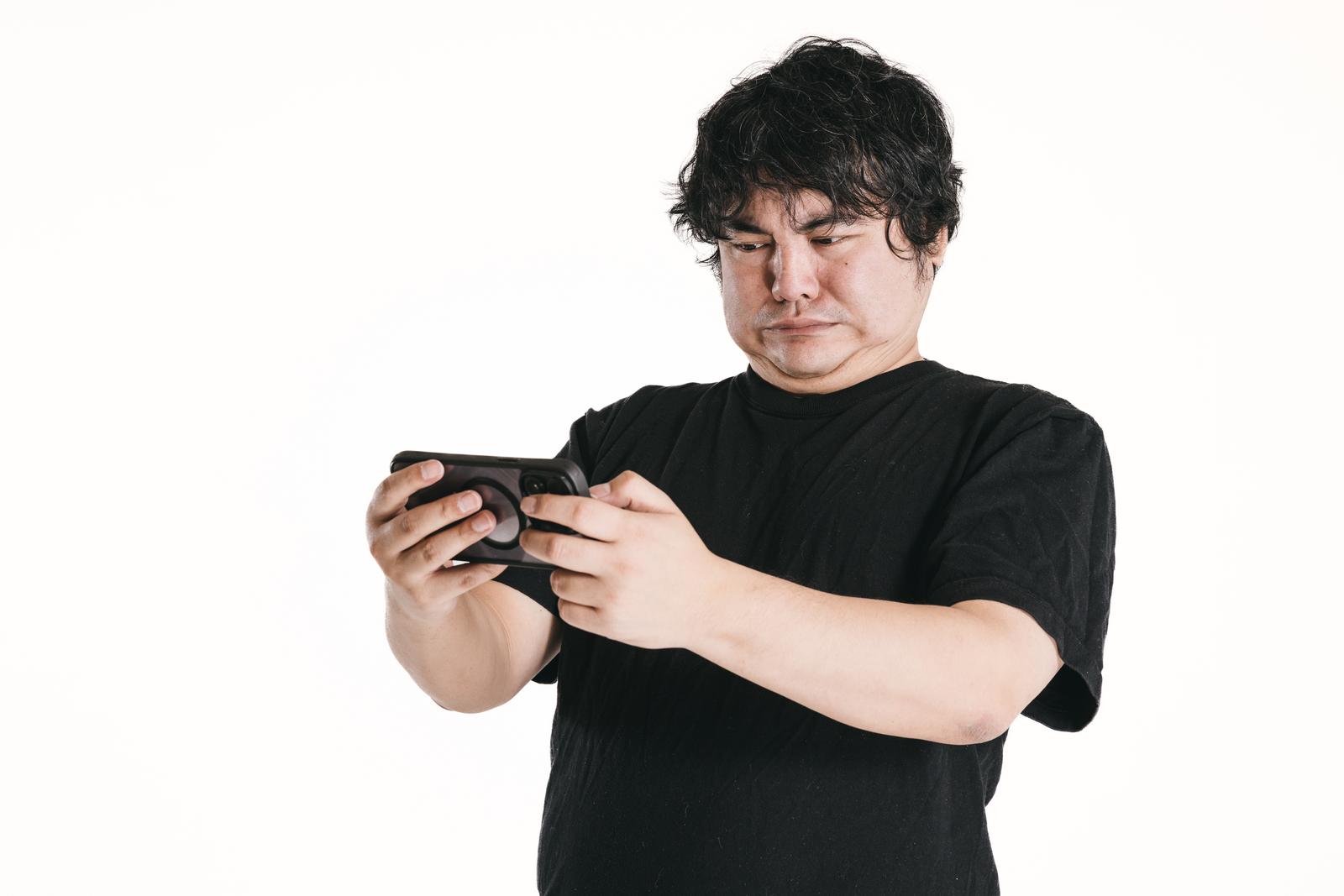 黒いTシャツを着た男性がスマートフォンの画面に見入る真剣な表情［モデル：段田隼人］