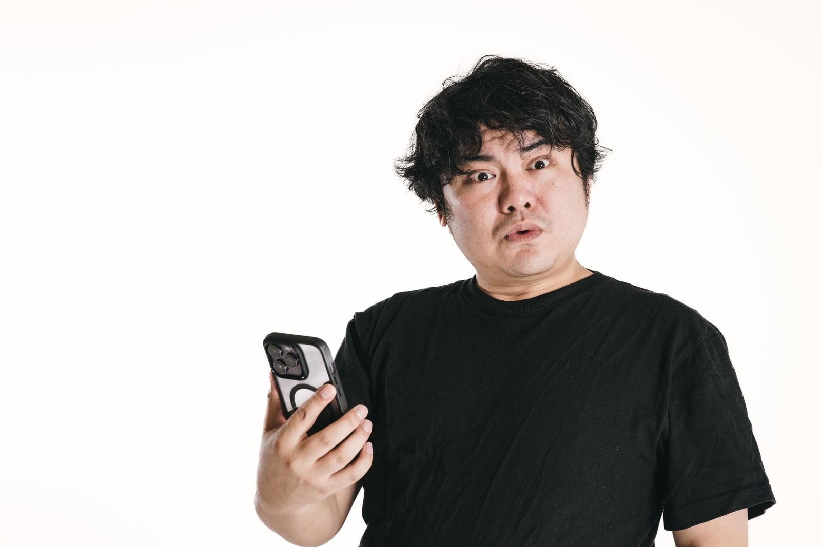 スマホを持ち目を丸くして驚く黒いTシャツの男性［モデル：段田隼人］