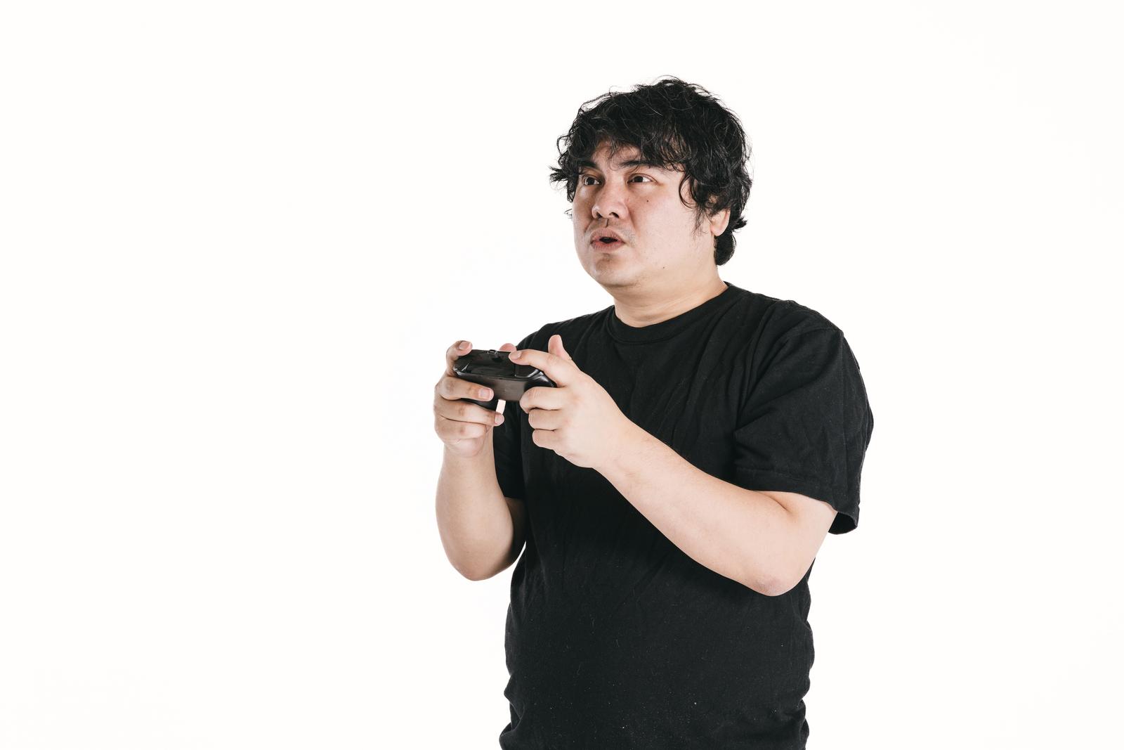 ゲームコントローラーを握りしめて画面を見つめる男性の真剣な表情［モデル：段田隼人］