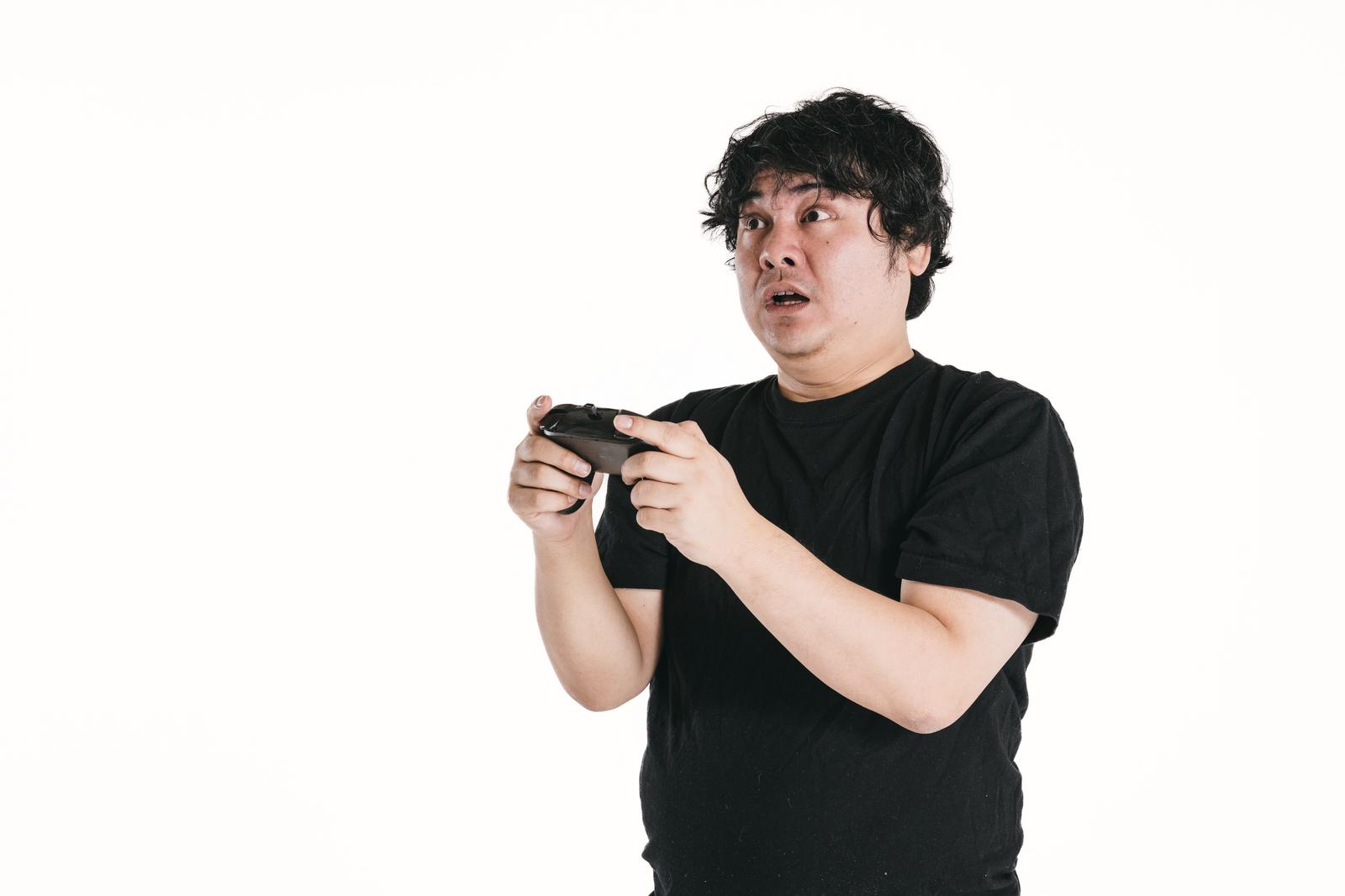 ゲームコントローラーを握りながら驚いた表情をする男性［モデル：段田隼人］