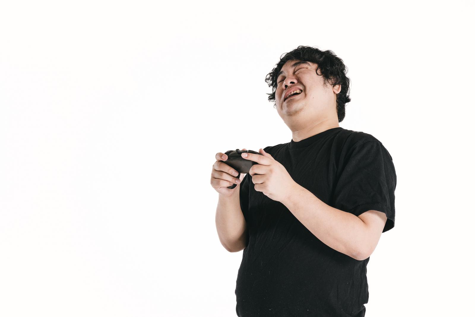 黒いTシャツを着た男性がゲームコントローラーを握り、苦い表情で上を向いている［モデル：段田隼人］