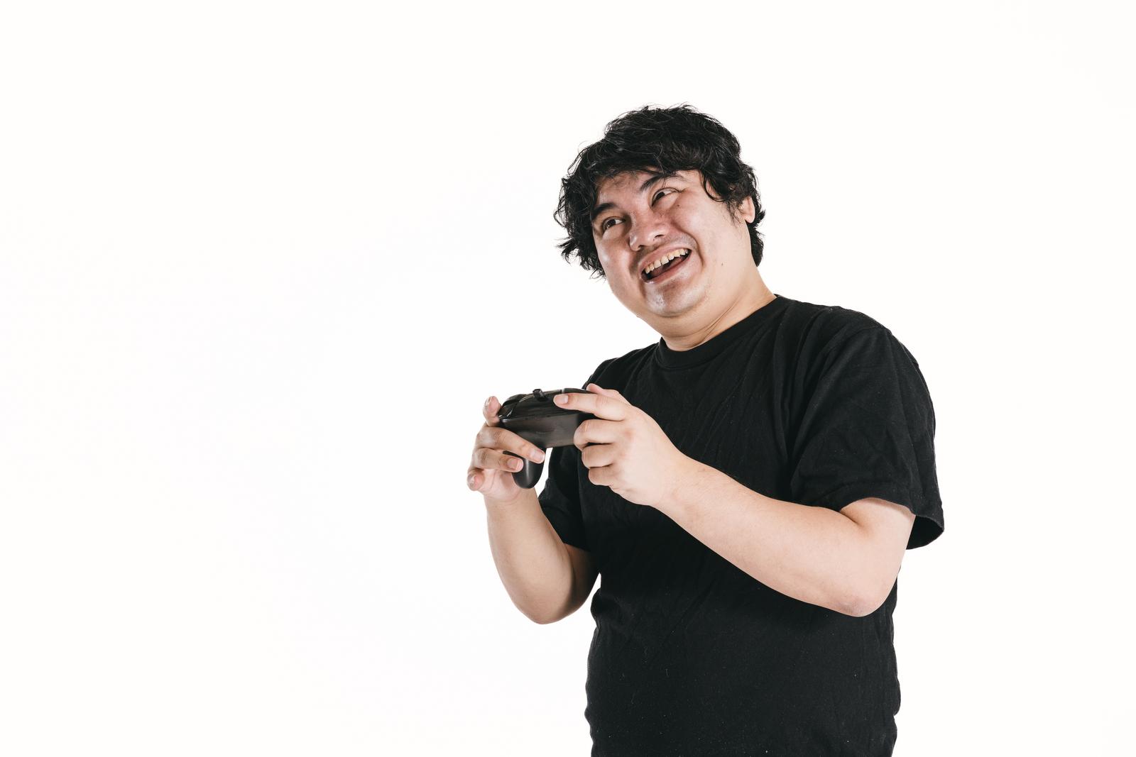 ゲームコントローラーを握りながら笑顔を浮かべる黒いTシャツの男性［モデル：段田隼人］