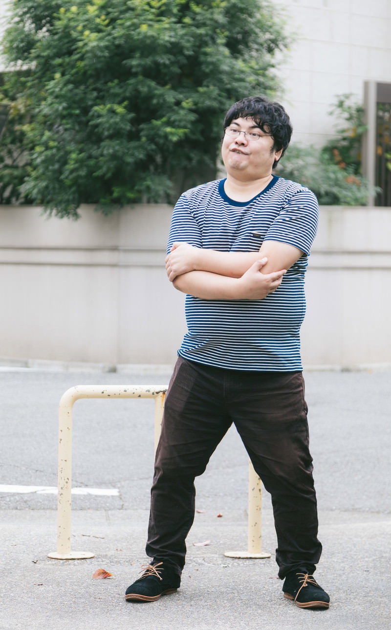 腕組みをして立つグレーのTシャツを着た男性［モデル：段田隼人］