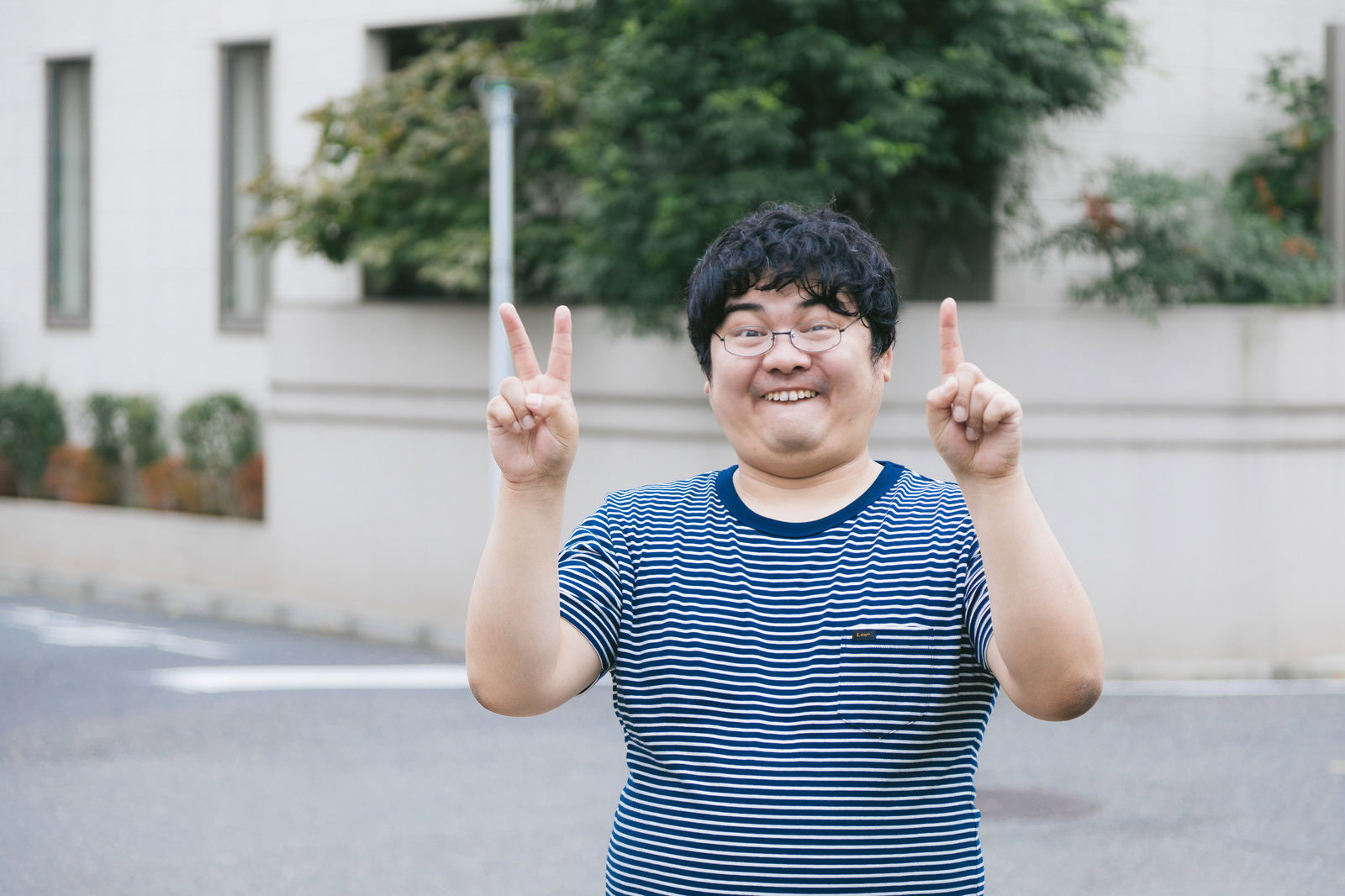 両手でピースサインをして笑顔を見せる青いボーダーシャツの男性［モデル：段田隼人］
