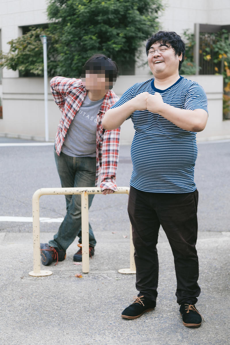 駐車場で拳を握りしめて立つ青いTシャツの男性
