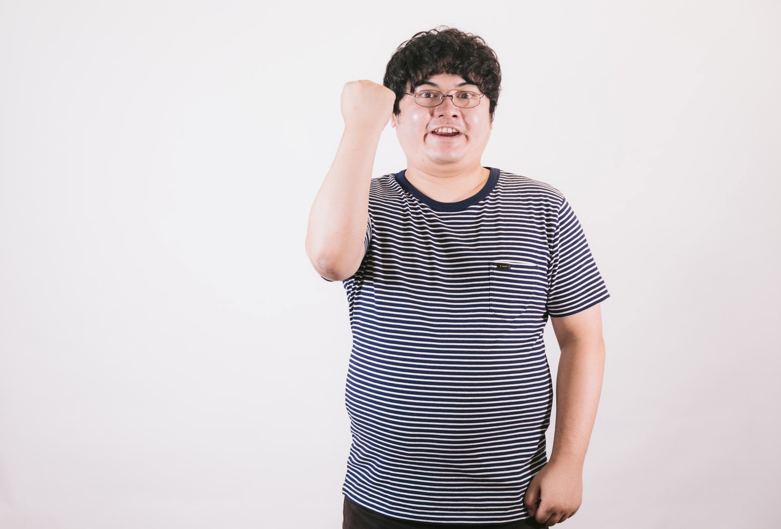 紺白ボーダーのTシャツを着た眼鏡の男性が、片手を頭に当て拳を構えて笑顔でポーズを取っている［モデル：段田隼人］
