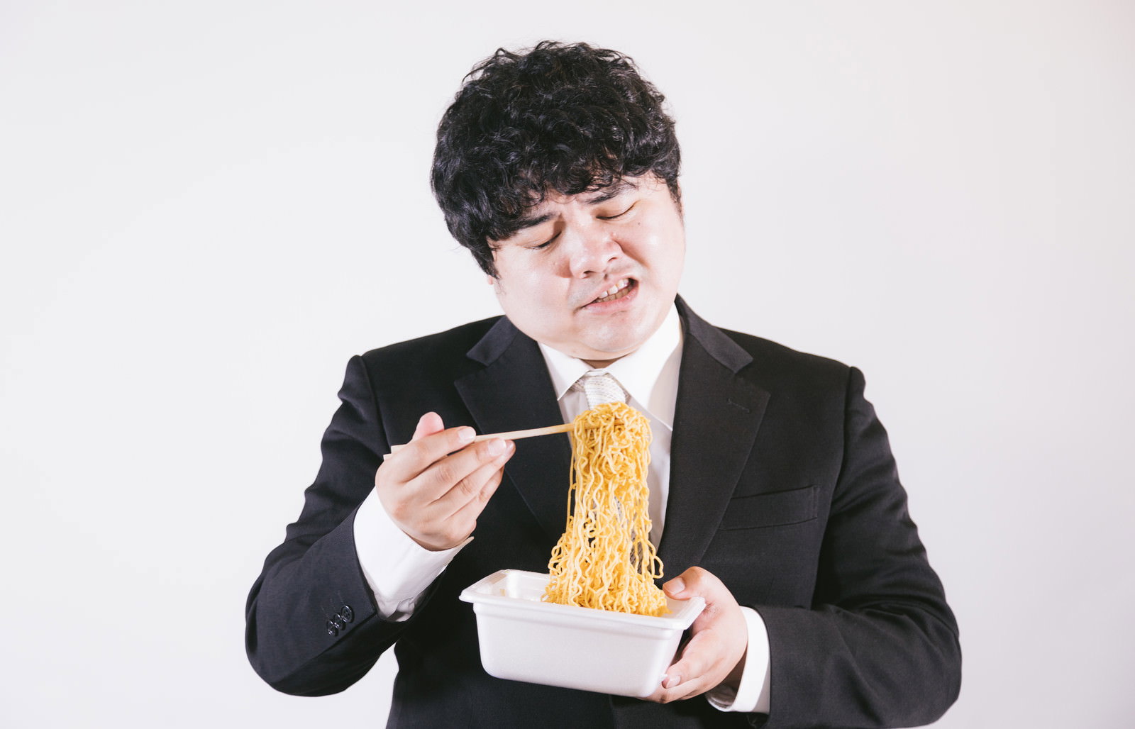 スーツの男性がカップ焼きそばを食べる［モデル：段田隼人］