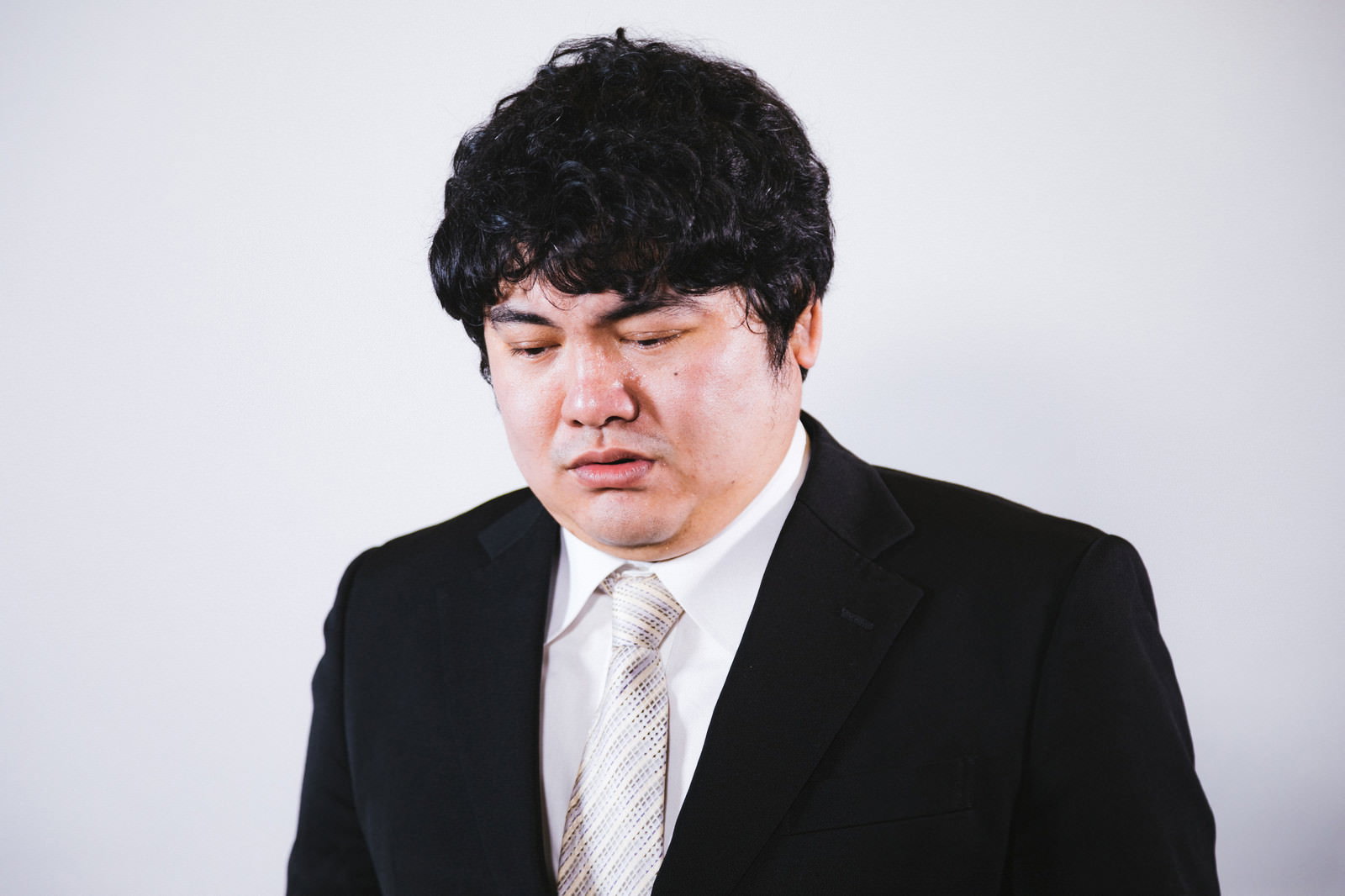 黒いスーツを着て肩を落として落ち込んでいる男性会社員［モデル：段田隼人］