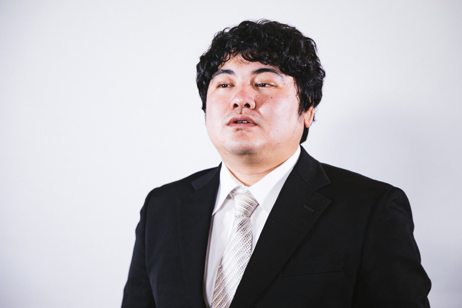 黒いスーツを着た男性がインタビューに答えている様子［モデル：段田隼人］