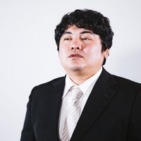 インタビューに答える黒いスーツ姿の会社員男性の写真