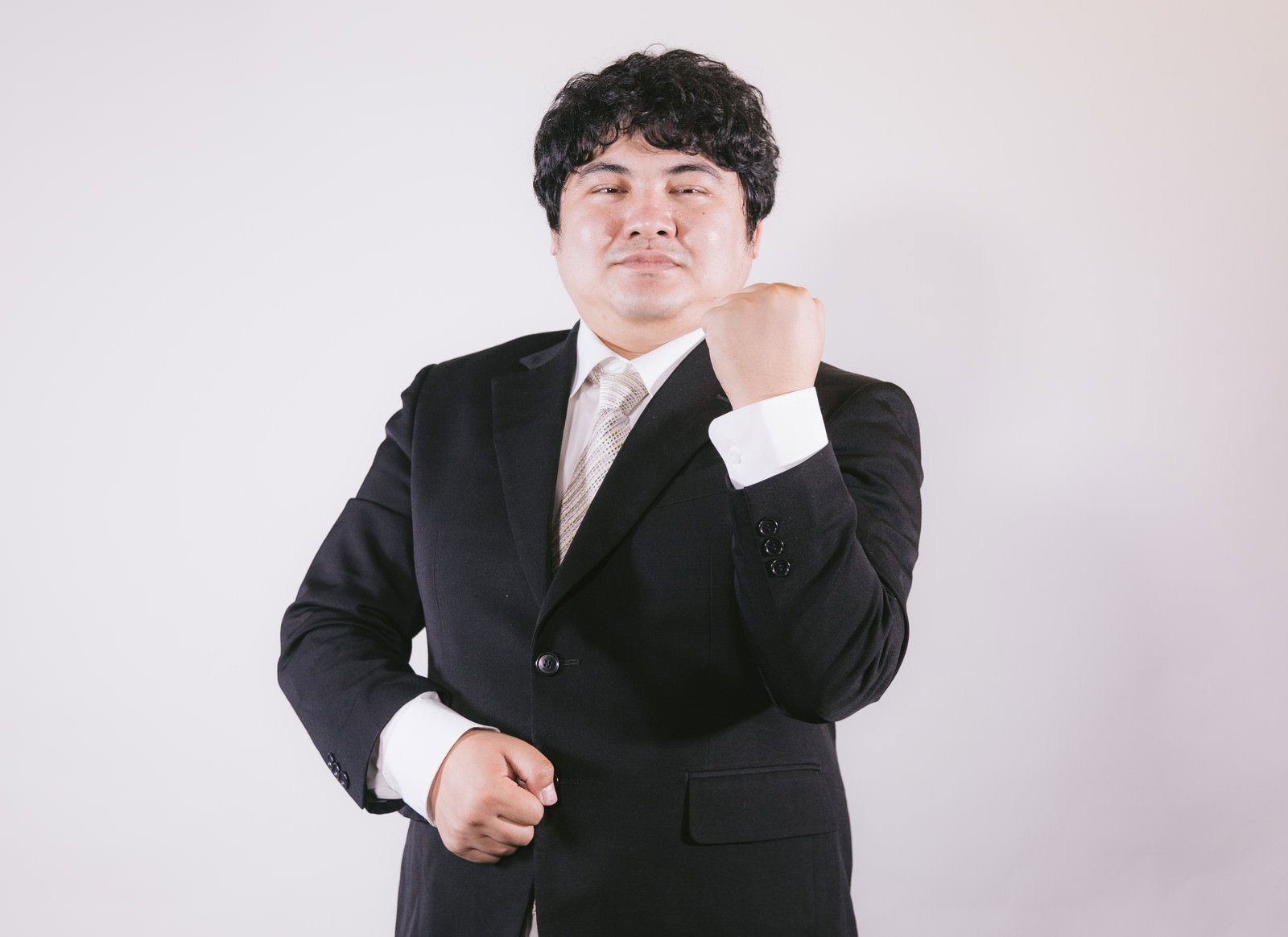 黒いスーツを着た男性が手をあごに当てて自信に満ちた表情でポーズを取っている［モデル：段田隼人］