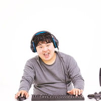 ヘッドセットをつけてパソコンでゲーム実況をする男性の写真