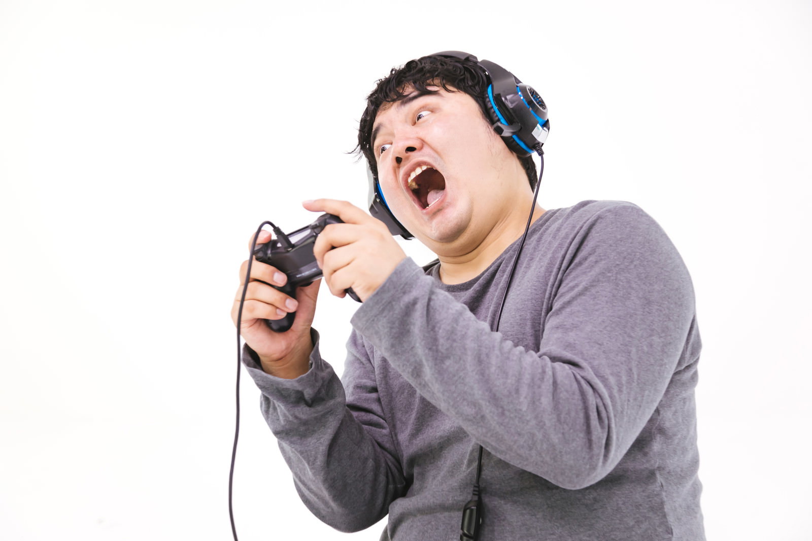 ヘッドセットを装着してコントローラーを握り、大きく口を開けて雄叫びを上げる男性［モデル：段田隼人］