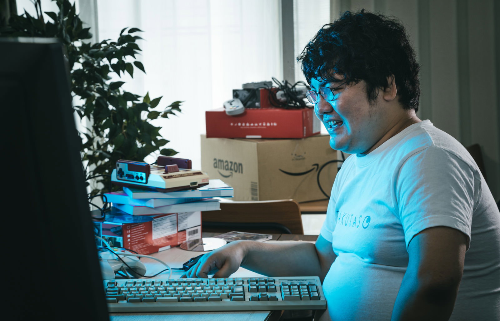 青いライティングに照らされたデスク環境で、キーボードに向かい怒った表情の男性［モデル：段田隼人］