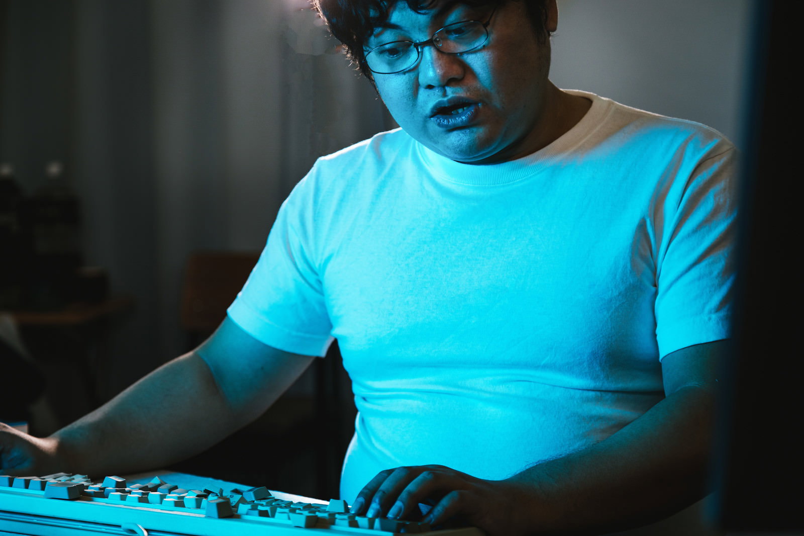 青い光の下でキーボードの破損を前にした男性エンジニア［モデル：段田隼人］