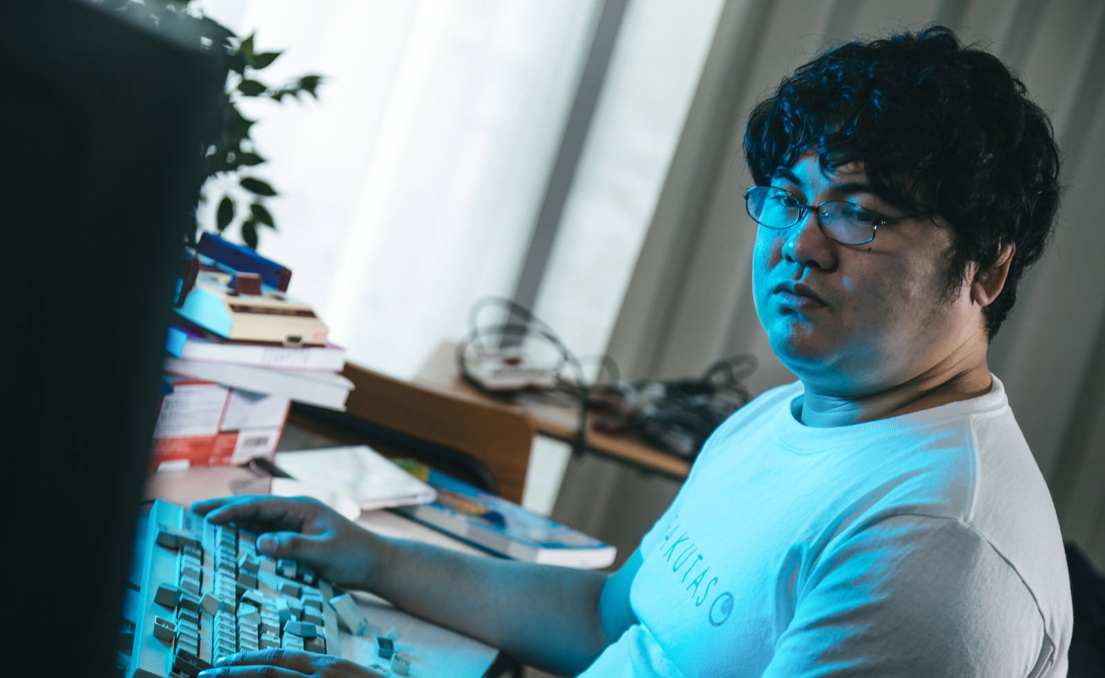 デスクに向かい、キーボードを前に困惑した表情を浮かべ画面を見つめる眼鏡姿の男性［モデル：段田隼人］