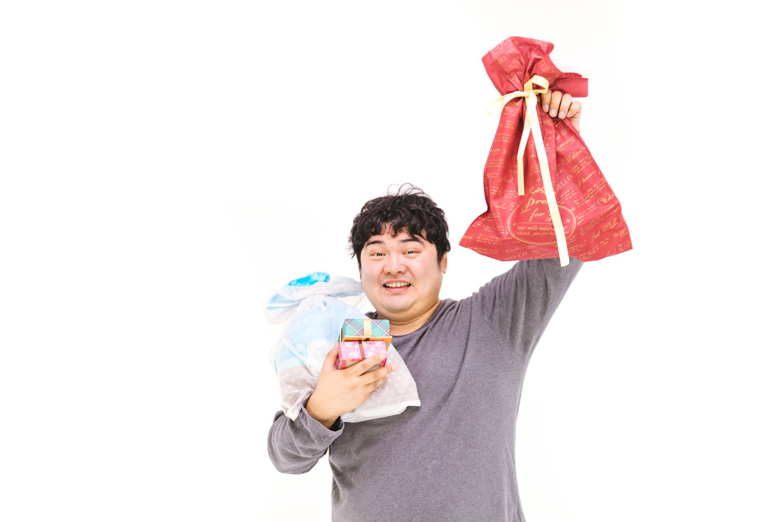 赤いリボンのついたプレゼント袋を持って喜ぶグレーのトップスの男性［モデル：段田隼人］