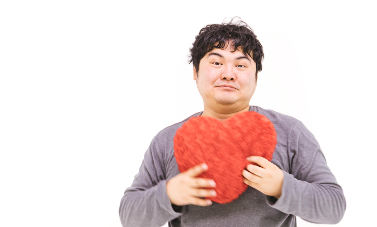 赤いハート型のクッションを胸に抱きしめる男性［モデル：段田隼人］