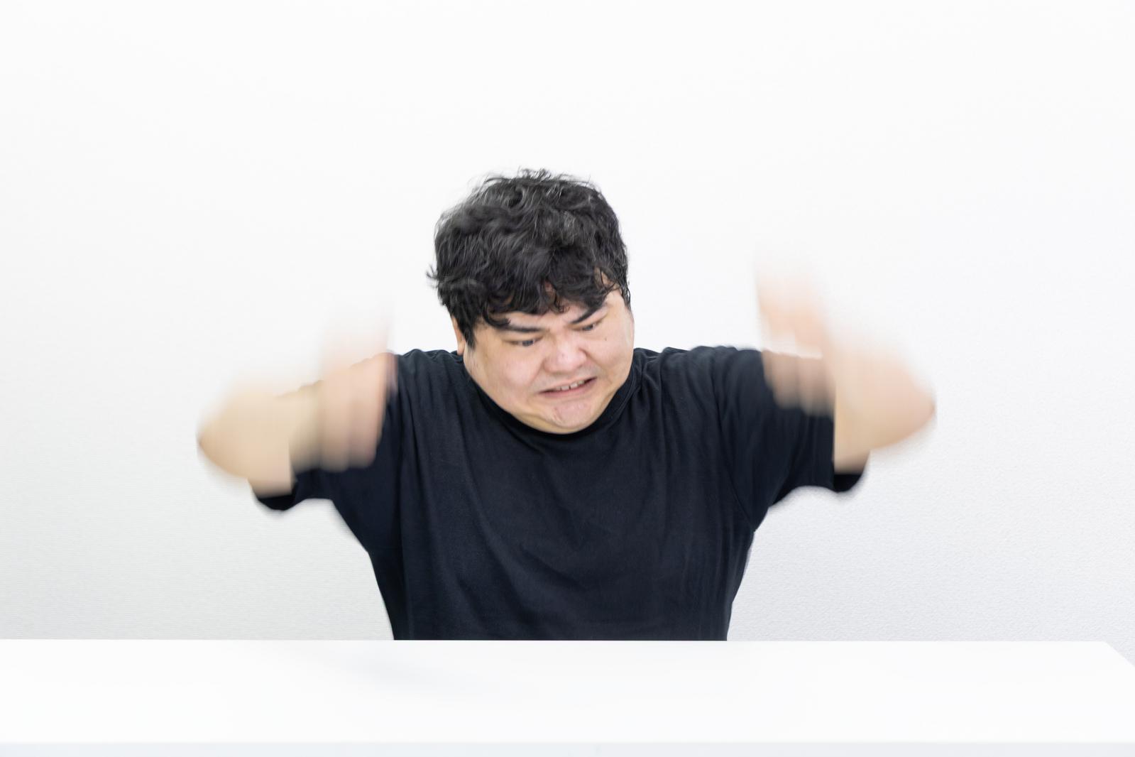 黒Tシャツの男性が両腕を振り上げて怒りの表情を見せている［モデル：段田隼人］