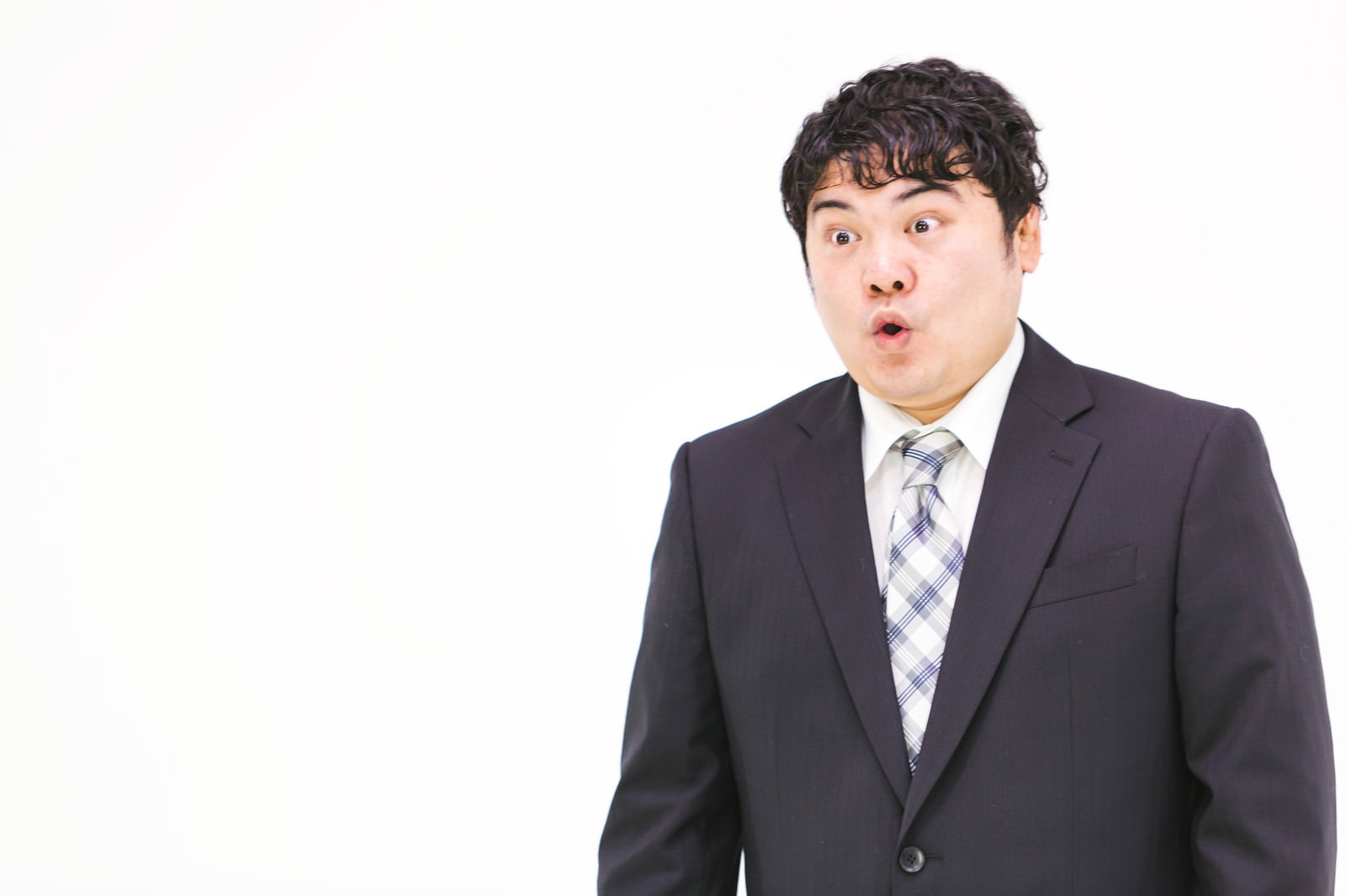 スーツを着た男性が目を丸くして驚いた表情をしている［モデル：段田隼人］