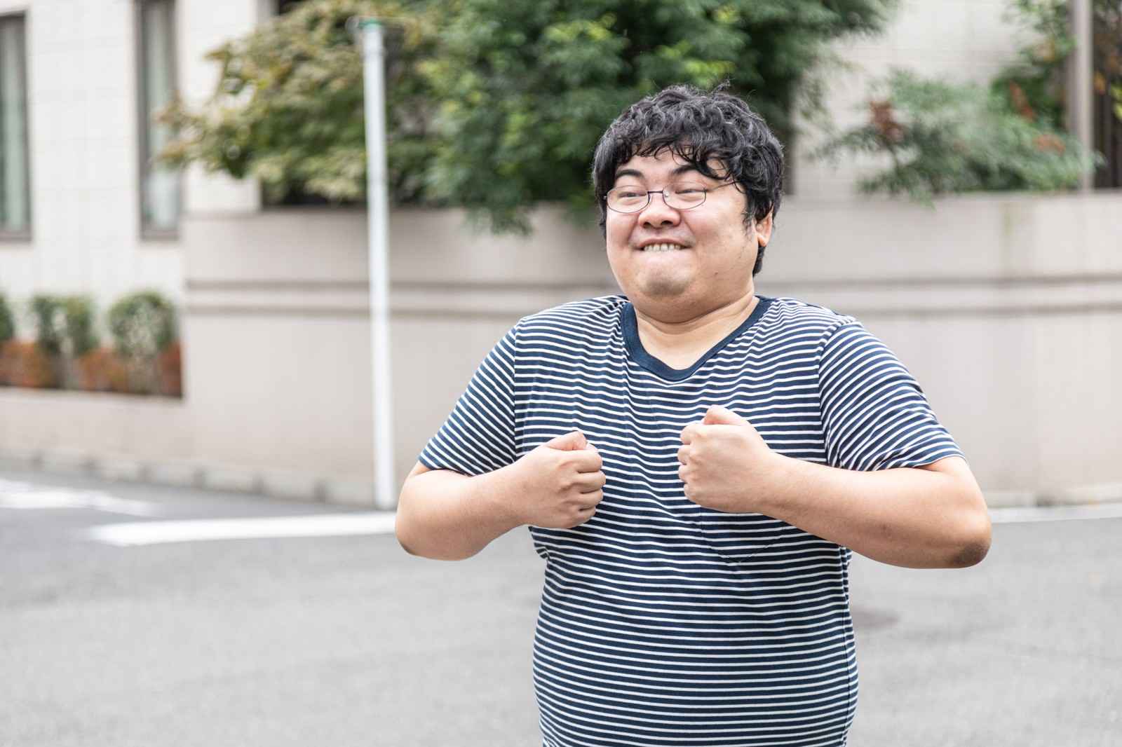 ボーダー柄のTシャツを着たメガネの男性が両手で握り拳を作り怒った表情［モデル：段田隼人］