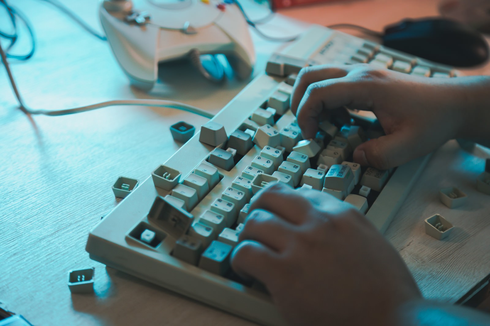 青い照明の下でキーボードを叩く手元のクローズアップ［モデル：段田隼人］