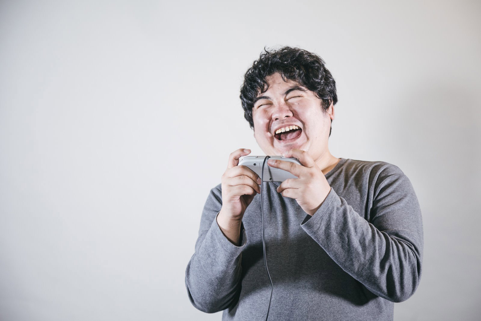 ゲームコントローラーを持って大笑いする男性［モデル：段田隼人］