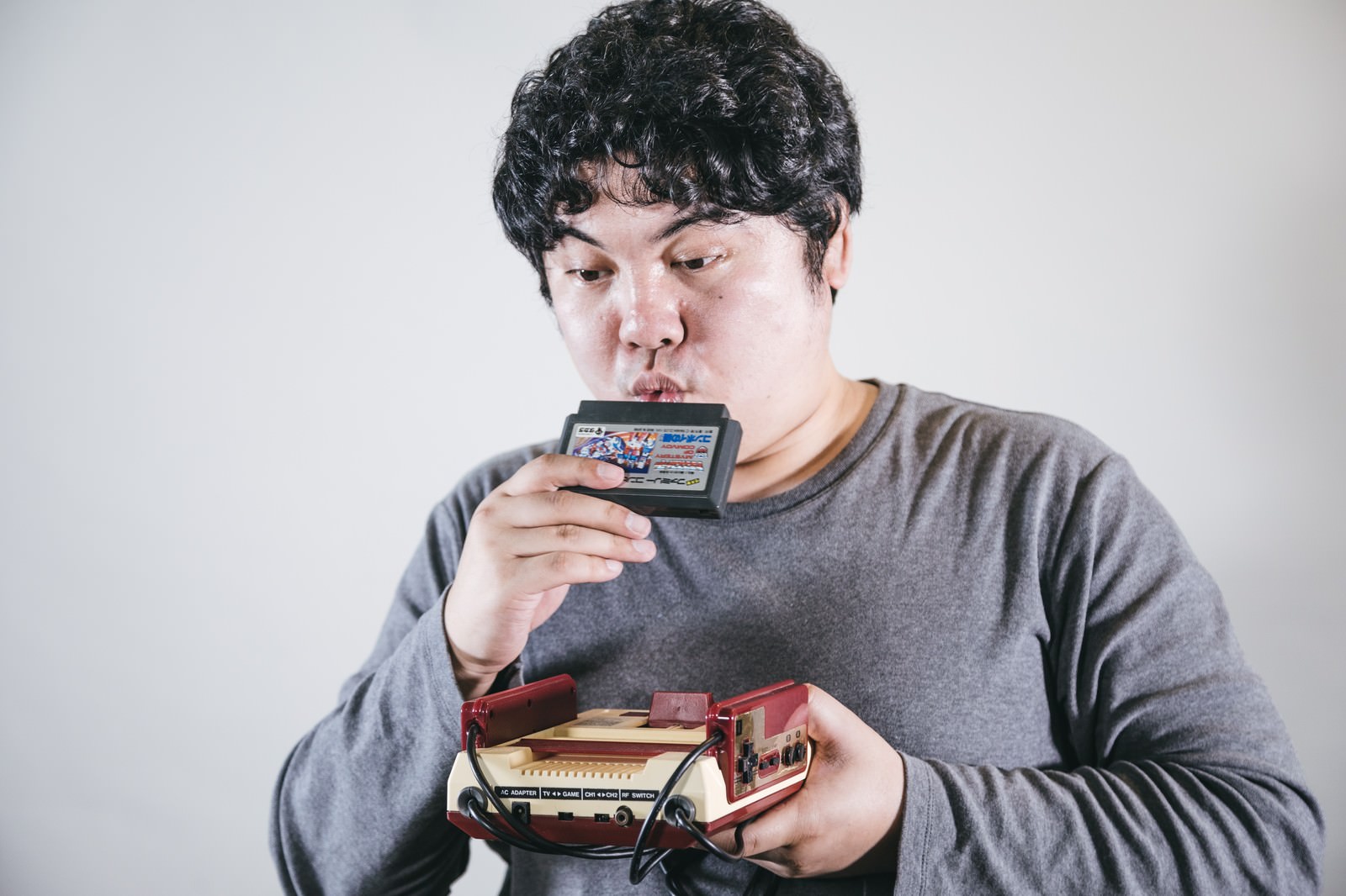 ファミコンのカセットに息をふぅーと吹きかけるゲーマー男性［モデル：段田隼人］