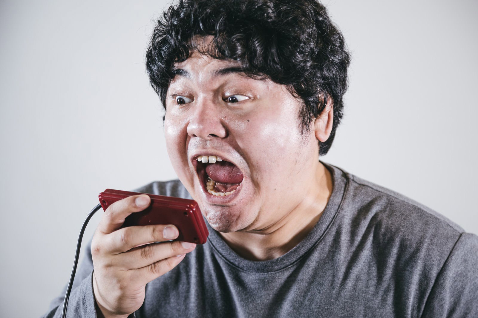 ゲームコントローラーを持って口を開けて叫んでいる男性［モデル：段田隼人］