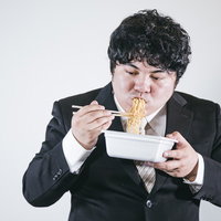 スーツを着てオフィスでカップ焼きそばを食べるビジネスマンの写真