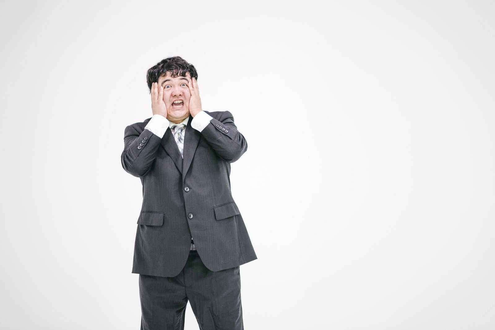 両手で顔を押さえ口を開けたスーツの男性［モデル：段田隼人］