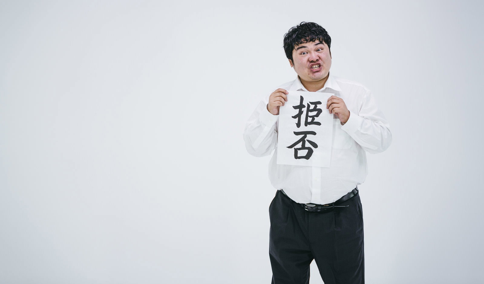 白いトレーナーを着た男性が扌臣否と書かれた紙を持って立っている［モデル：段田隼人］