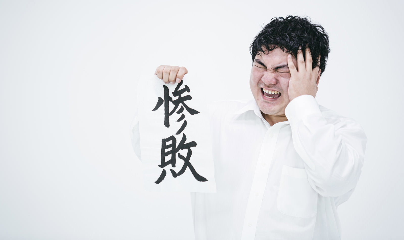 白い服を着た男性が両手で頭を抱えている様子［モデル：段田隼人］